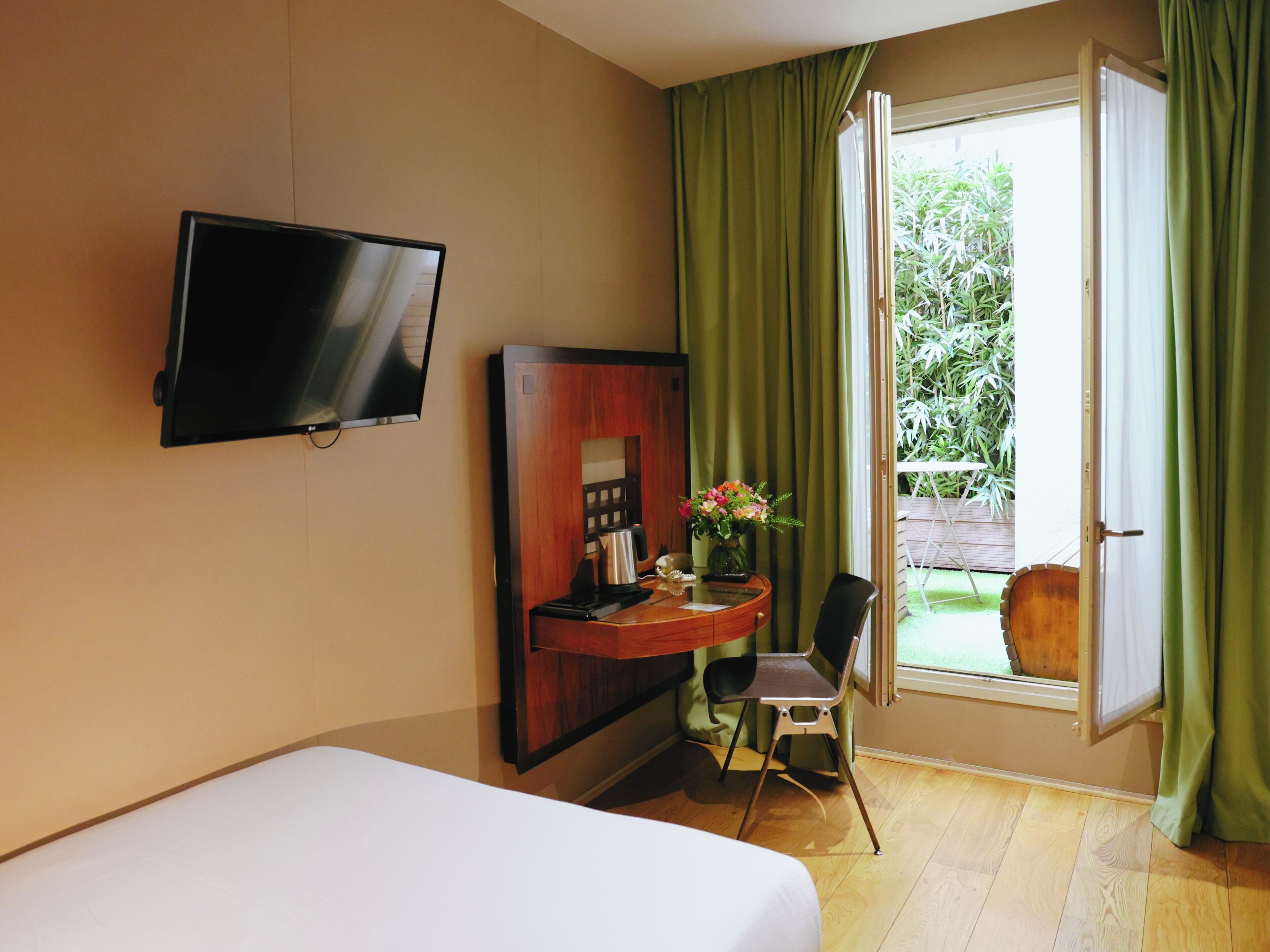 A hotel room with a bed, a desk with a chair, a television, and a window with curtains.