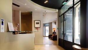 A hotel reception area with a reception desk, a framed picture on the wall, and a view of the street through large windows. - Hôtel Châteaudun Opéra (Paris)