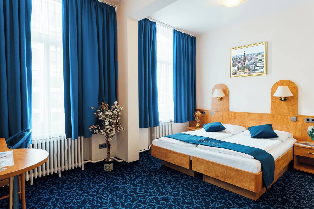 A hotel room with a large bed, a wooden headboard, a nightstand, a table, and a radiator.