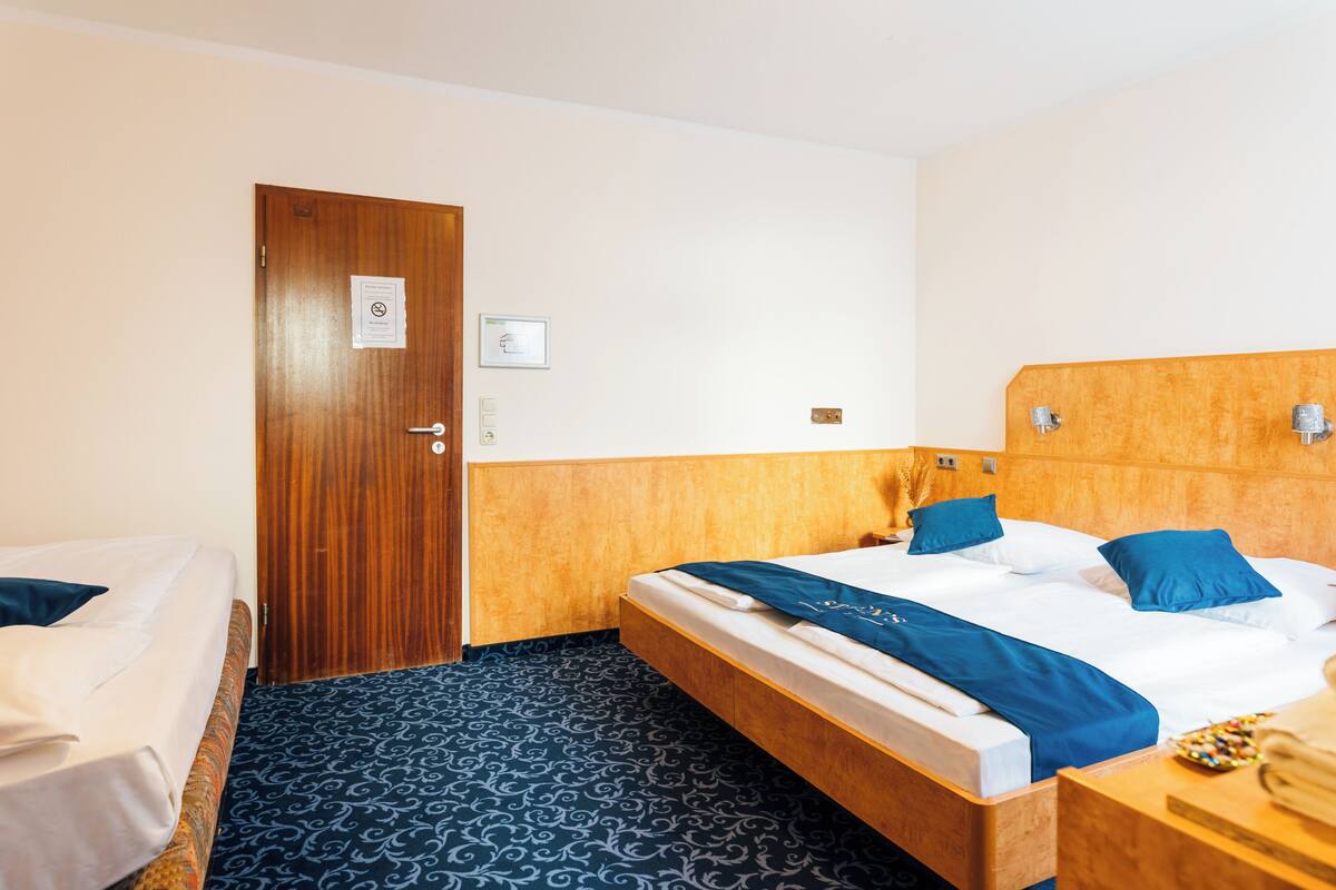 A hotel room with a wooden headboard, a bed with blue bedding, a bedside table with a lamp, and a patterned floor.