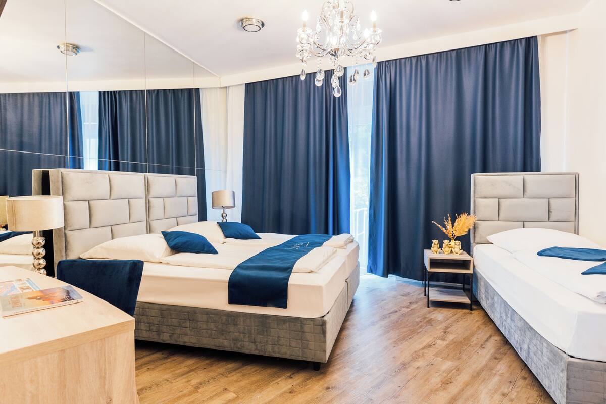 A modern hotel room with a large bed, a smaller bed, a desk, and a nightstand.