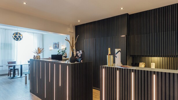 A modern reception area with a dark wood panel design, a reception desk, and a seating area with a table and chairs.