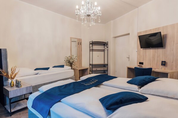 Una habitación de hotel con dos camas, un televisor montado en la pared, una araña y un escritorio con una silla.