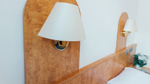 A wooden headboard with a white lampshade and a gold accent. - Steen's Hotel (Hamburg)