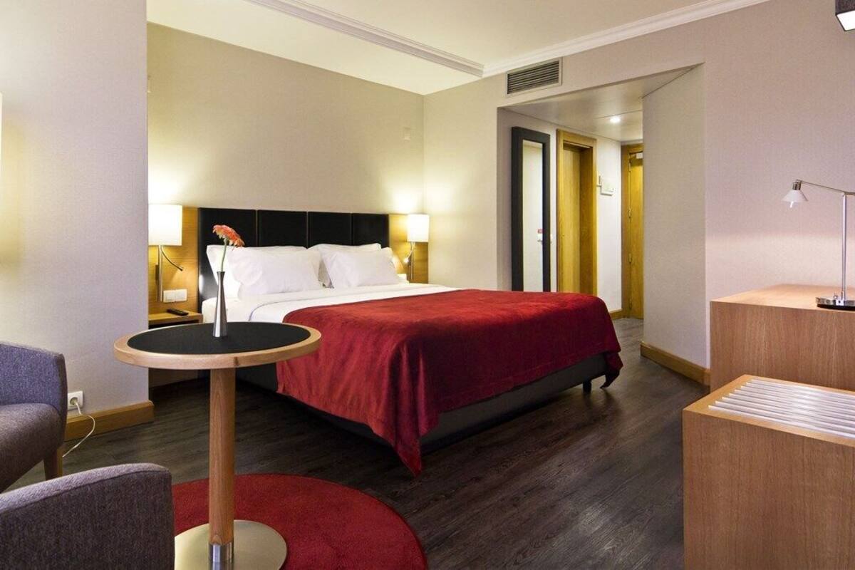 A hotel room with a bed, a round table, a chair, a lamp, and a bedside table.