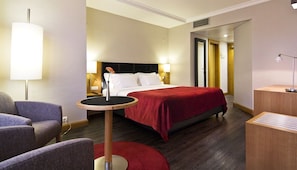 A hotel room with a bed, a round table, a chair, a lamp, and a bedside table. - SANA Reno Hotel (Lisbon)