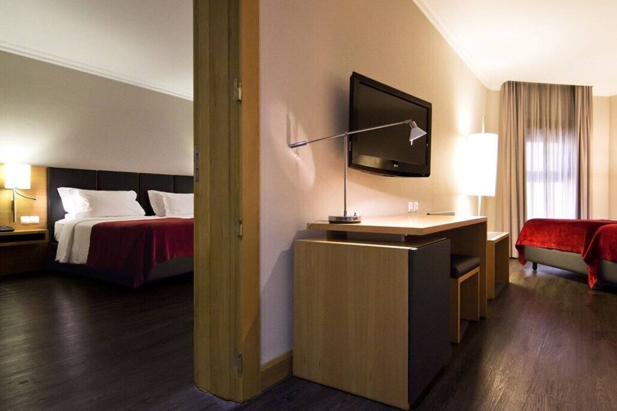 A hotel room with two beds, a desk, a TV, and a lamp.