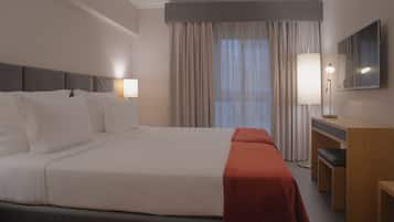 A hotel room with two beds, a desk, a chair, a lamp, and a large window with curtains.