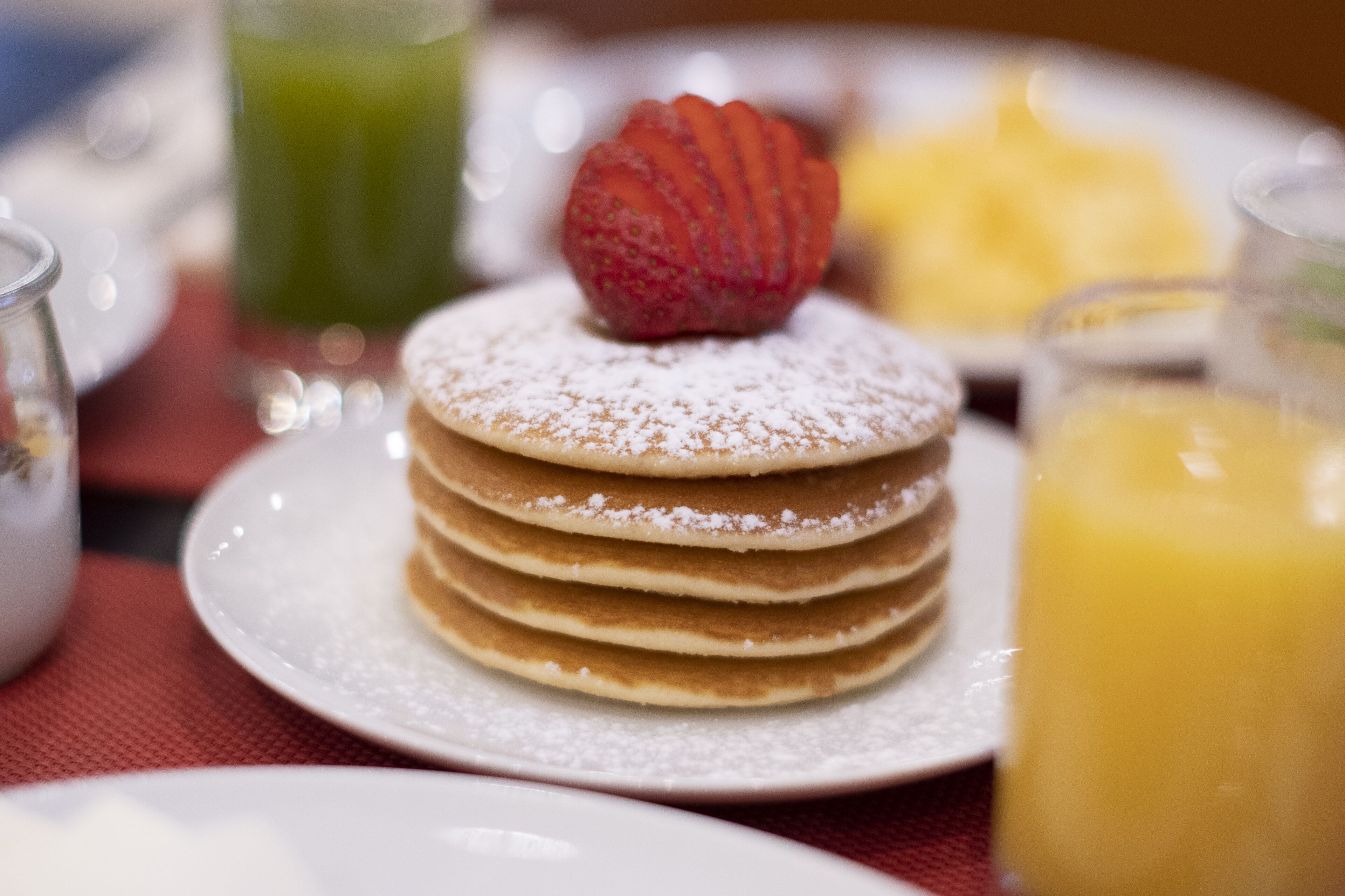 A stack of pancakes with powdered sugar and a strawberry on top, served on a white plate.