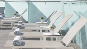 Eine Dachterrasse mit Liegestühlen und Topfpflanzen mit Blick auf eine Stadtlandschaft.