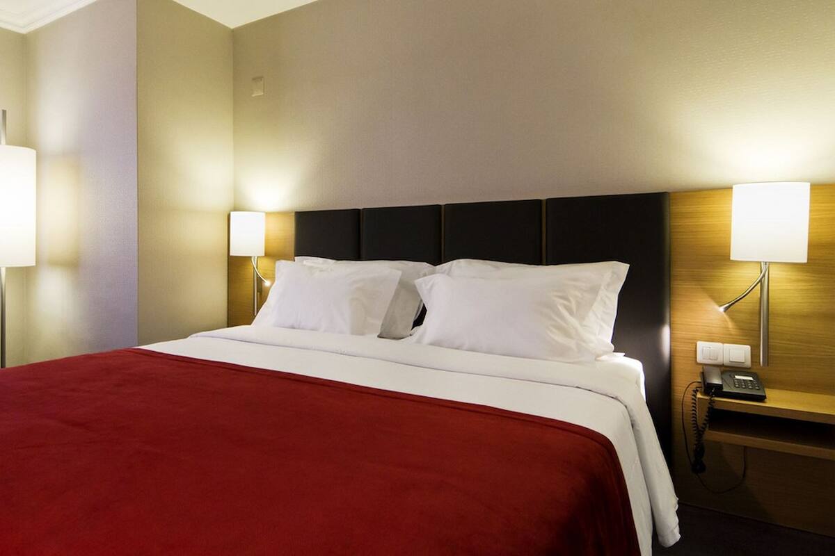 A hotel room with a large bed, two bedside lamps, a nightstand with a phone, and a chair.
