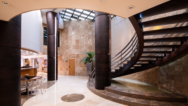 Eine geräumige Lobby mit einer geschwungenen Treppe, Marmorböden und einer Sitzecke mit Stühlen.