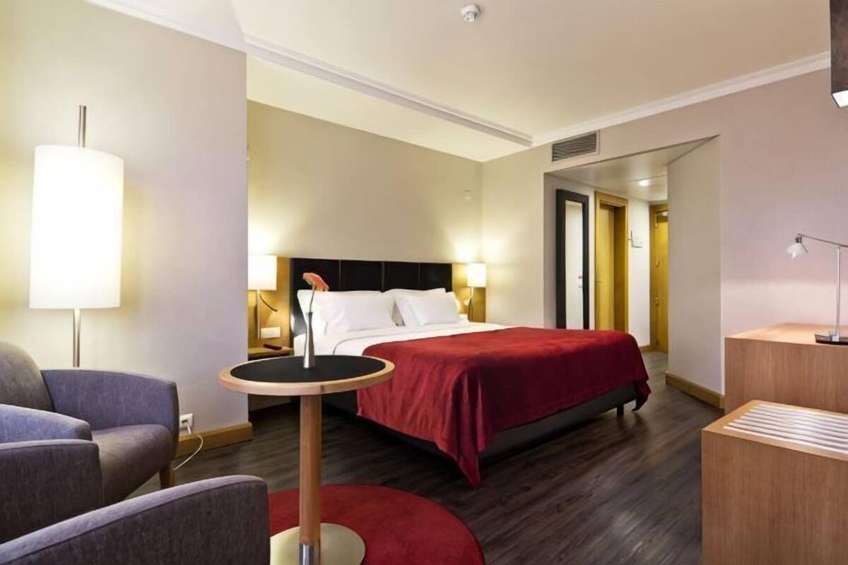 A hotel room with a bed, bedside tables, a chair, a lamp, and a desk.