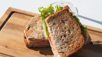 Un sándwich sobre una tabla de madera, con un cóctel al fondo.