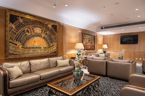 A hotel lobby with a leather sofa, a coffee table, a painting, a television, and a lamp.
