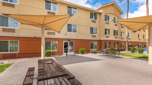 A hotel courtyard with outdoor seating, palm trees, and a building with multiple windows and air conditioning vents.