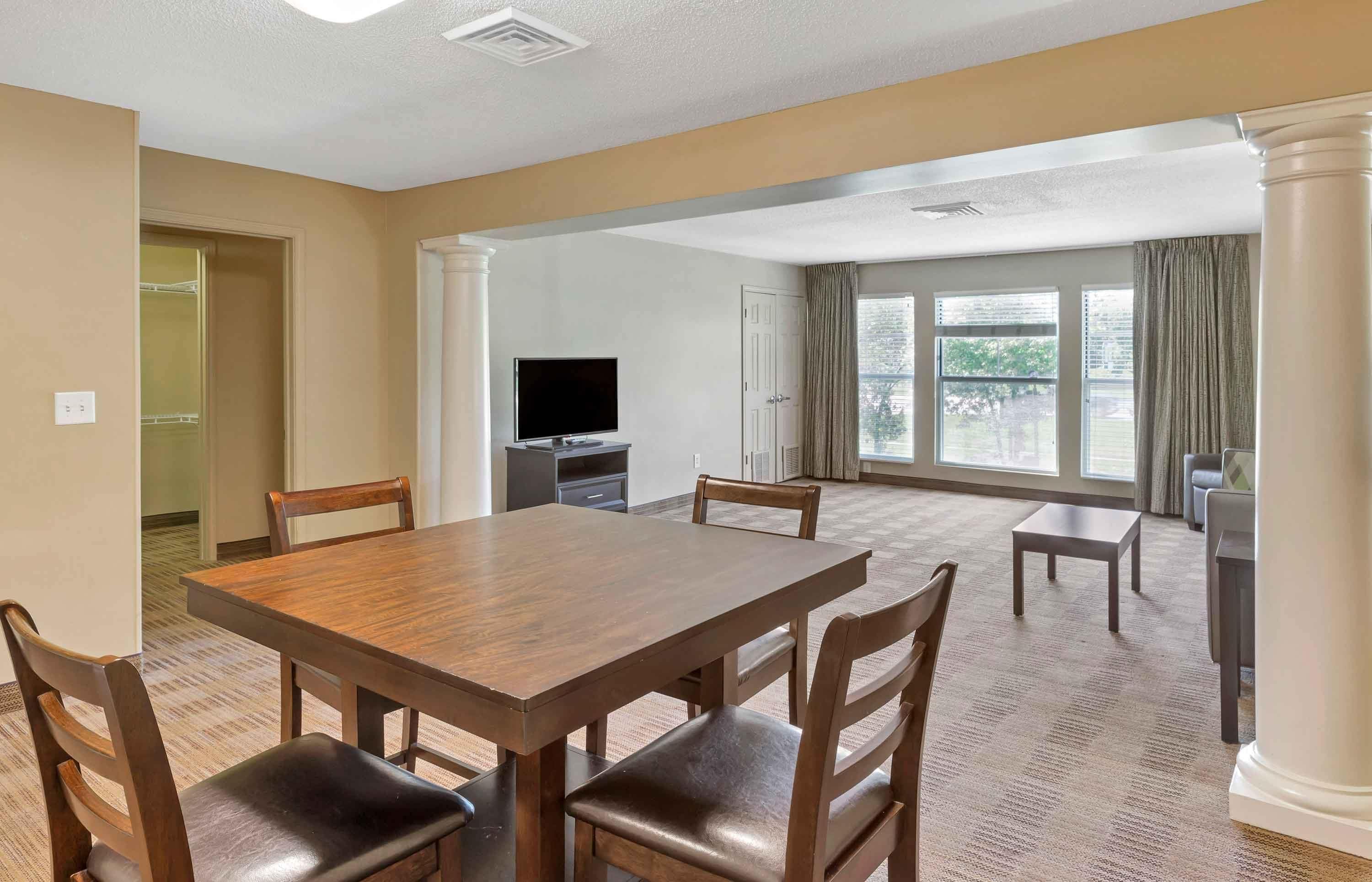 A spacious room with a large dining table, chairs, a flat-screen TV, and a large window with curtains.