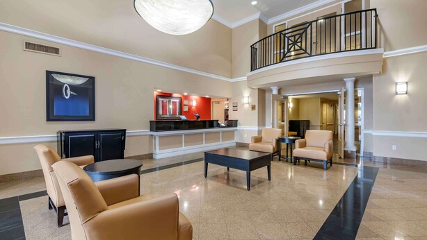Un amplio vestíbulo con mostrador de recepción, zona de estar y escalera a un nivel superior.