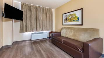 A living room with a brown leather sofa, a mounted flat-screen TV, a radiator, and a framed picture on the wall.