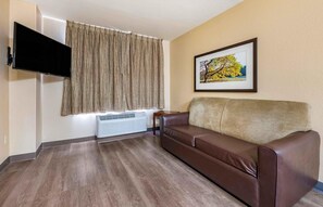 A living room with a brown leather sofa, a mounted flat-screen TV, a radiator, and a framed picture on the wall. - Extended Stay America Suites Orlando Southpark Commodity Cir (Orlando)