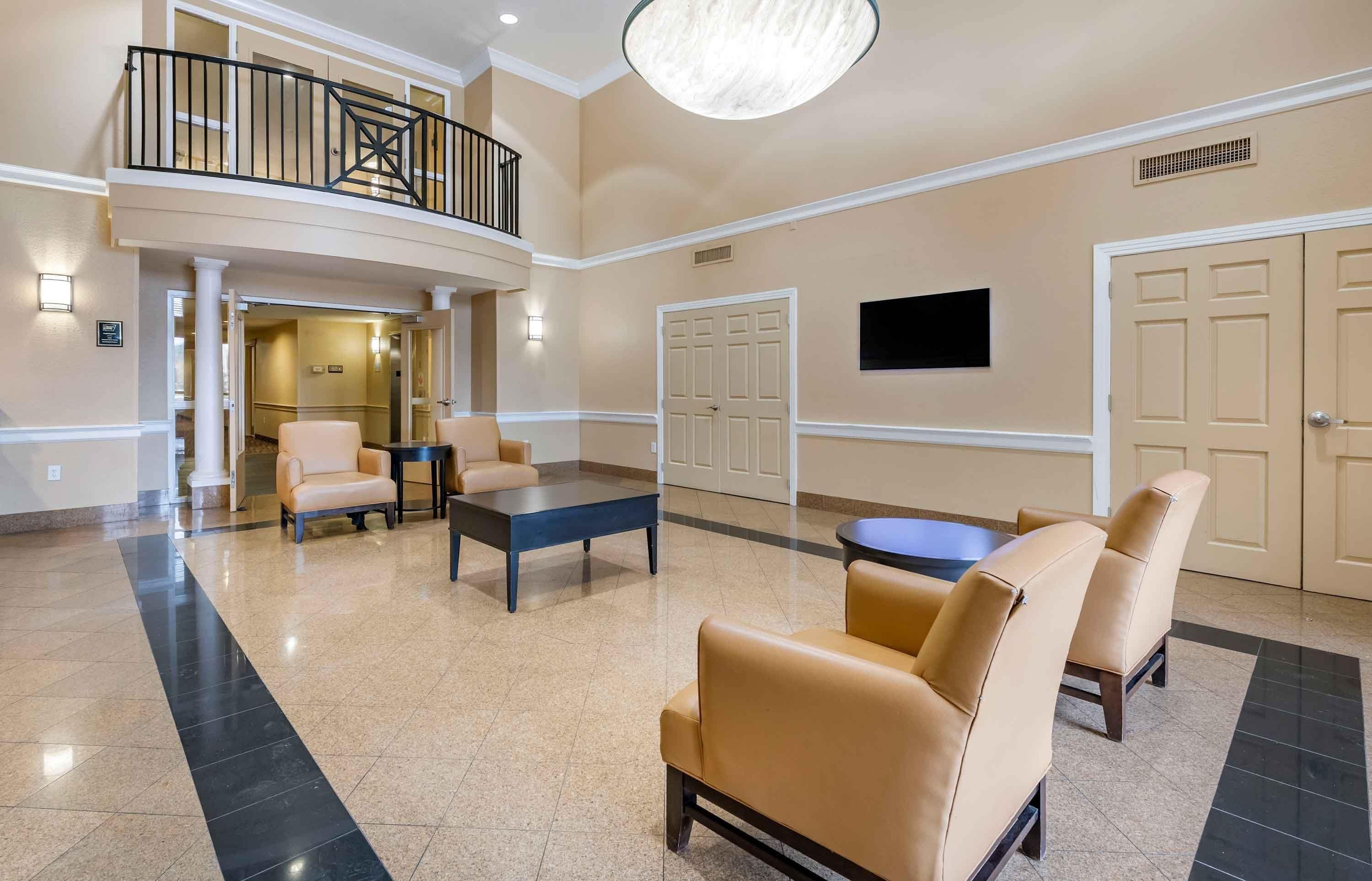 A hotel lobby with a seating area, a staircase, and a flat-screen TV mounted on the wall.