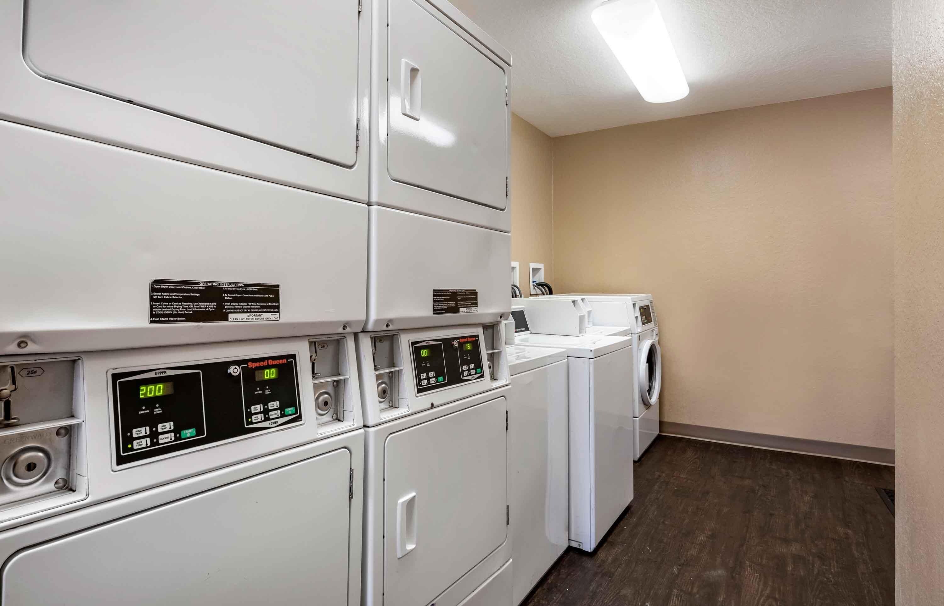 A laundry facility with stacked dryers and a washing machine, featuring control panels and operating instructions.