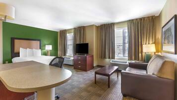 Una habitación de hotel con cama, escritorio, sofá, televisor y ventana con cortinas.