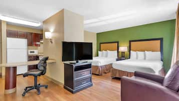 A hotel room with a kitchenette, a TV, a desk, and two beds.
