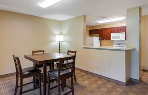 A compact hotel room with a dining table, four chairs, a small kitchenette, and a single floor lamp. - Extended Stay America Suites Orlando Southpark Commodity Cir (Orlando)