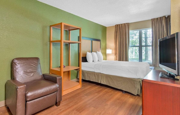 Habitación de hotel con cama, televisor, una silla y un estante de madera.