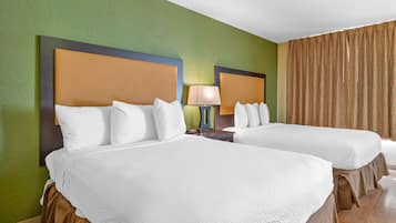 A hotel room with two beds, a nightstand with a lamp, and a curtain.