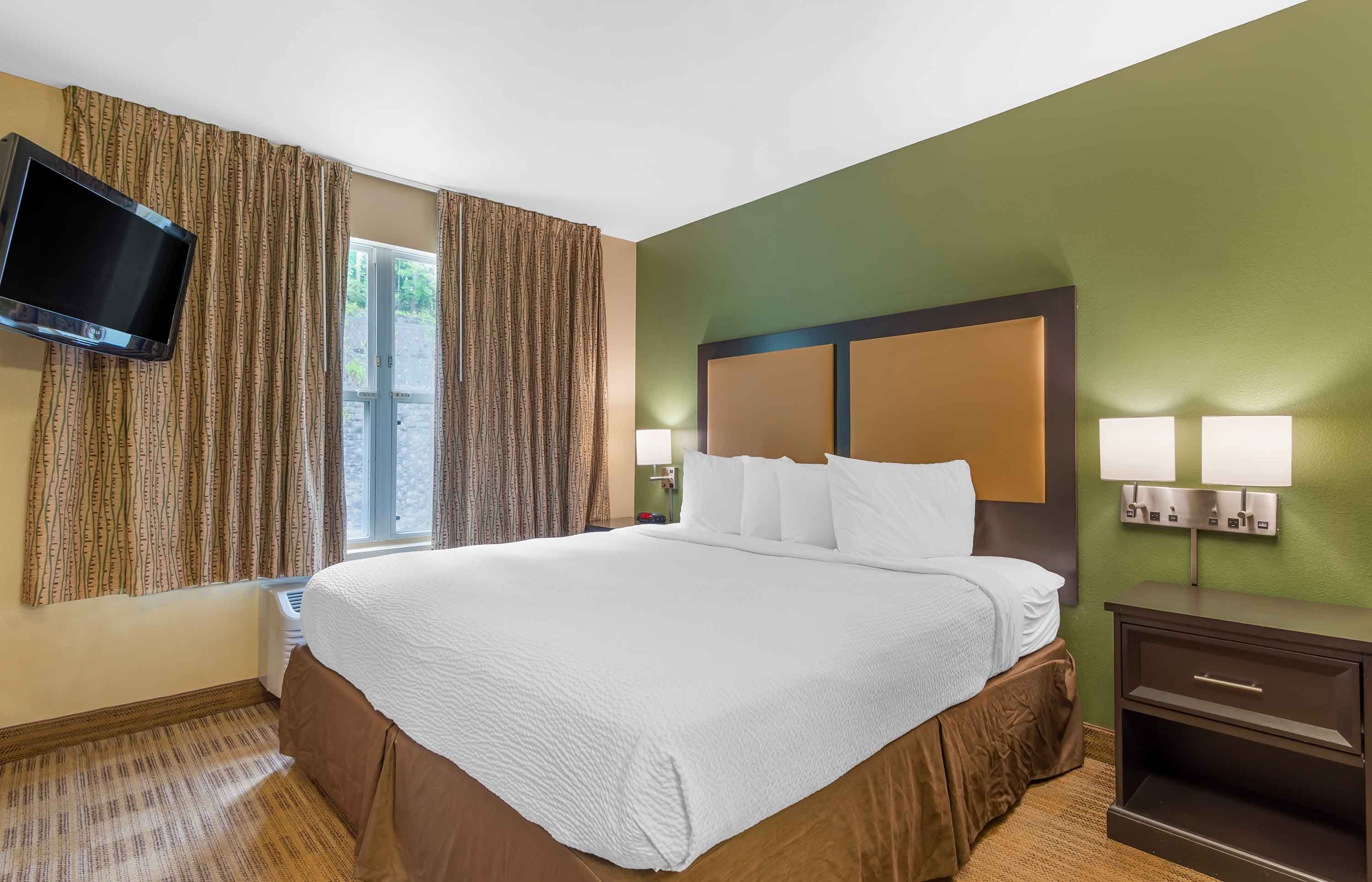 Een hotelkamer met een bed, gordijnen, een televisie en een nachtkastje.