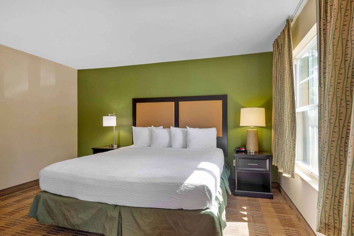 A hotel room with a large bed, two bedside tables, a window with curtains, and a green wall.
