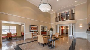 A spacious lobby with a high ceiling, a reception desk, and a staircase leading to an upper level. - Extended Stay America Suites Indianapolis Northwest I465 (Indianapolis)