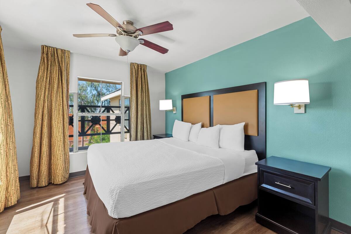 Une chambre d’hôtel avec un lit, une table de chevet, un ventilateur de plafond et une vue par la fenêtre.
