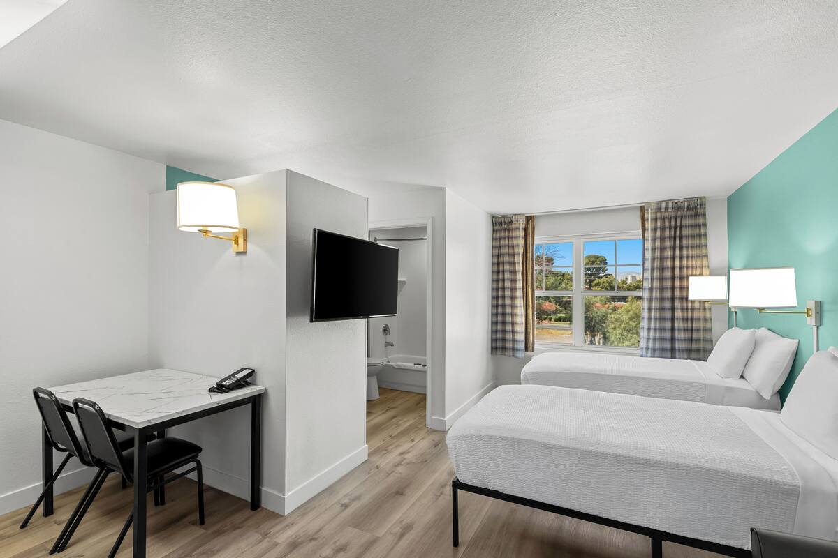 Une chambre d’hôtel équipée d’un bureau, de deux lits, d’une télévision et d’une fenêtre avec des rideaux.