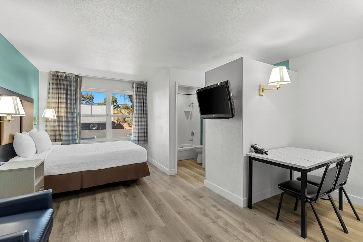 Une chambre d’hôtel avec un lit, un bureau, une chaise, une télévision et une fenêtre avec des rideaux.