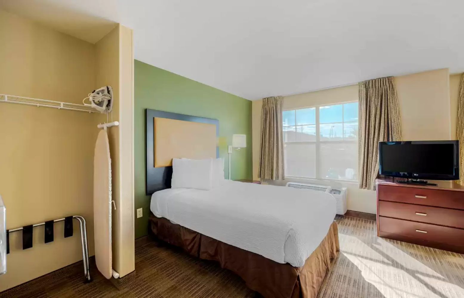 Une chambre d’hôtel comprenant un lit, une télévision, une fenêtre avec des rideaux et un espace douche.