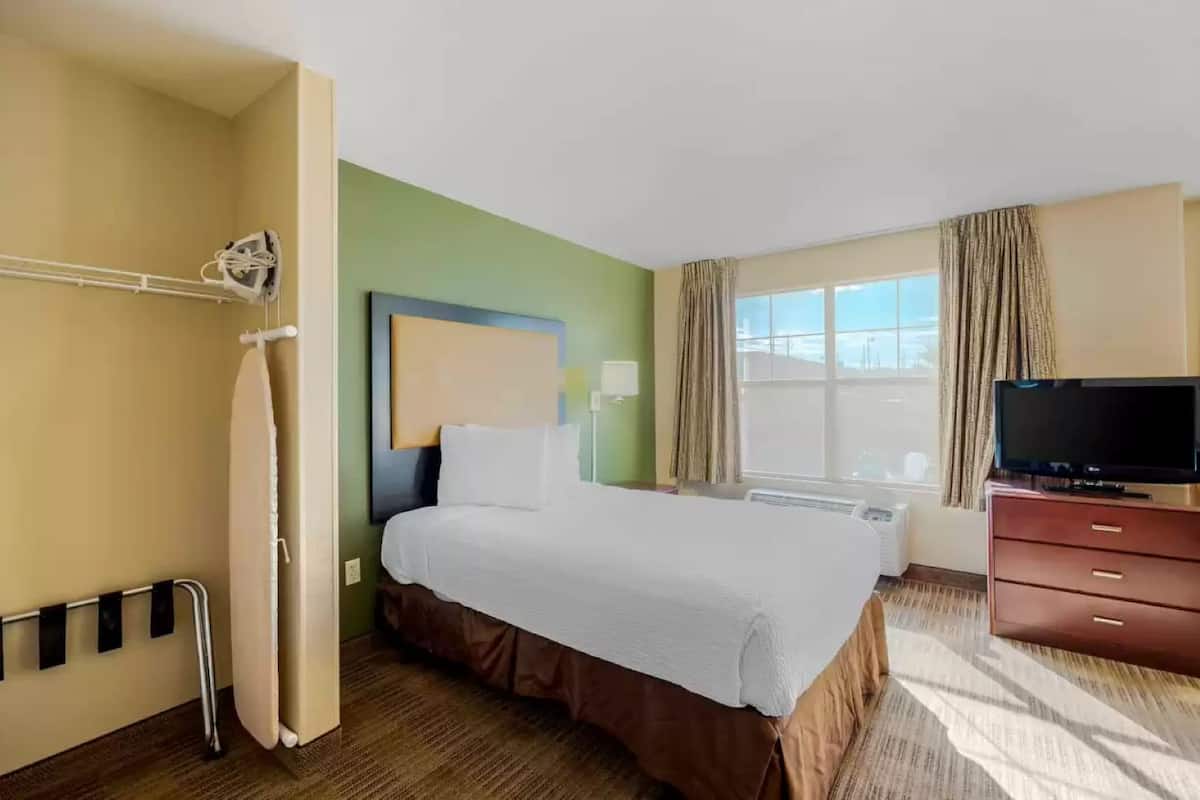A hotel room with a bed, a television, a window with curtains, and a shower area.