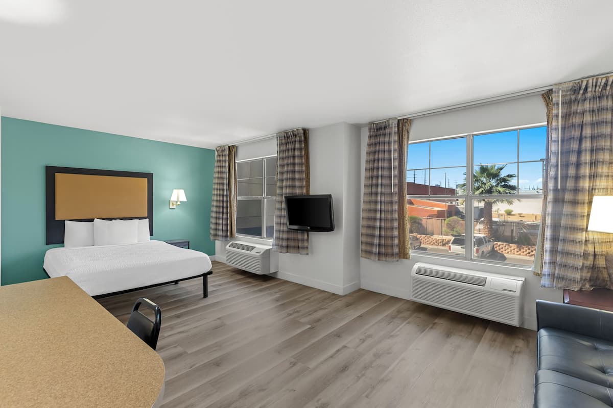 Une chambre d’hôtel avec un lit, un bureau, une télévision et de grandes fenêtres équipées de rideaux.