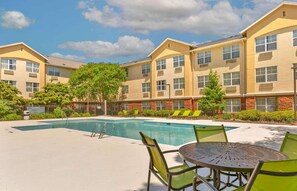A hotel courtyard with a swimming pool, lounge chairs, and a table.