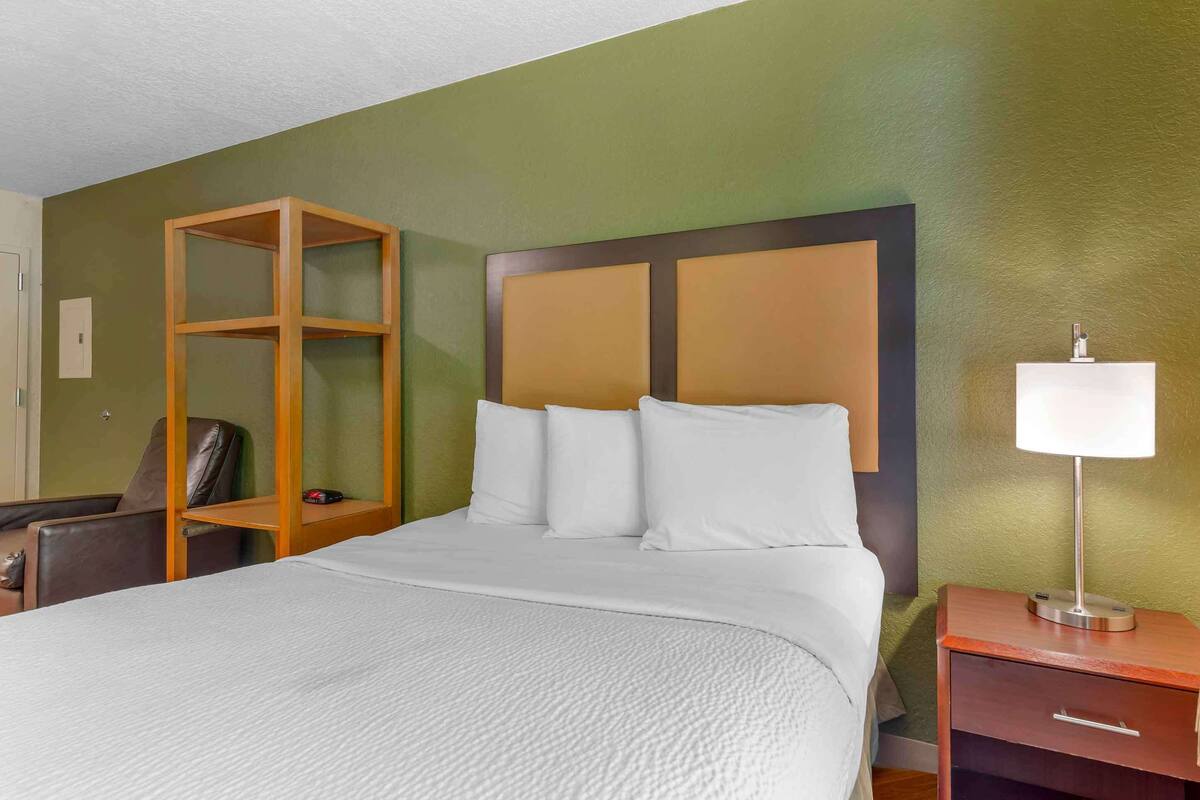 Ein Hotelzimmer mit einem Bett, einer Holzkonsolenwand, einem Schreibtisch mit Lampe und einem Sessel.