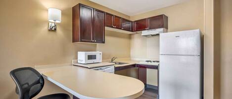 A compact kitchen with a microwave, refrigerator, and a small dining area with a chair.