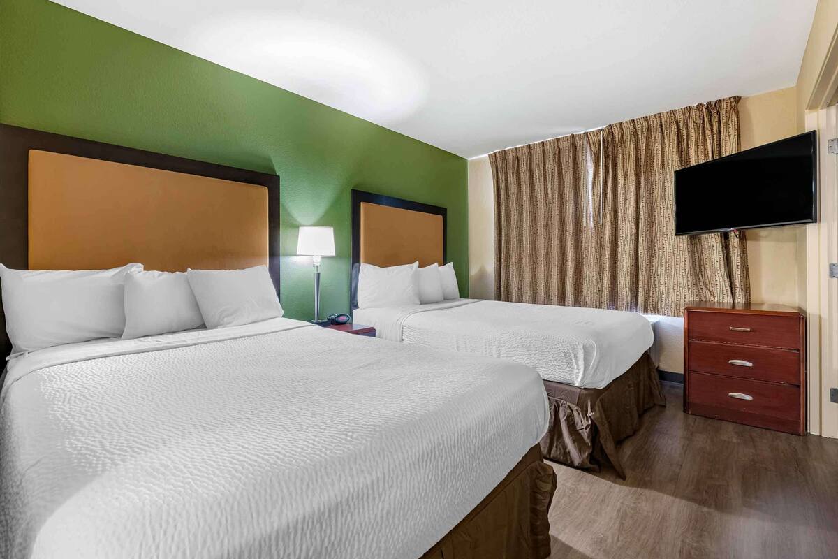 Ein Hotelzimmer mit zwei Betten, einem Fernseher, einer Lampe und einem Schminktisch.