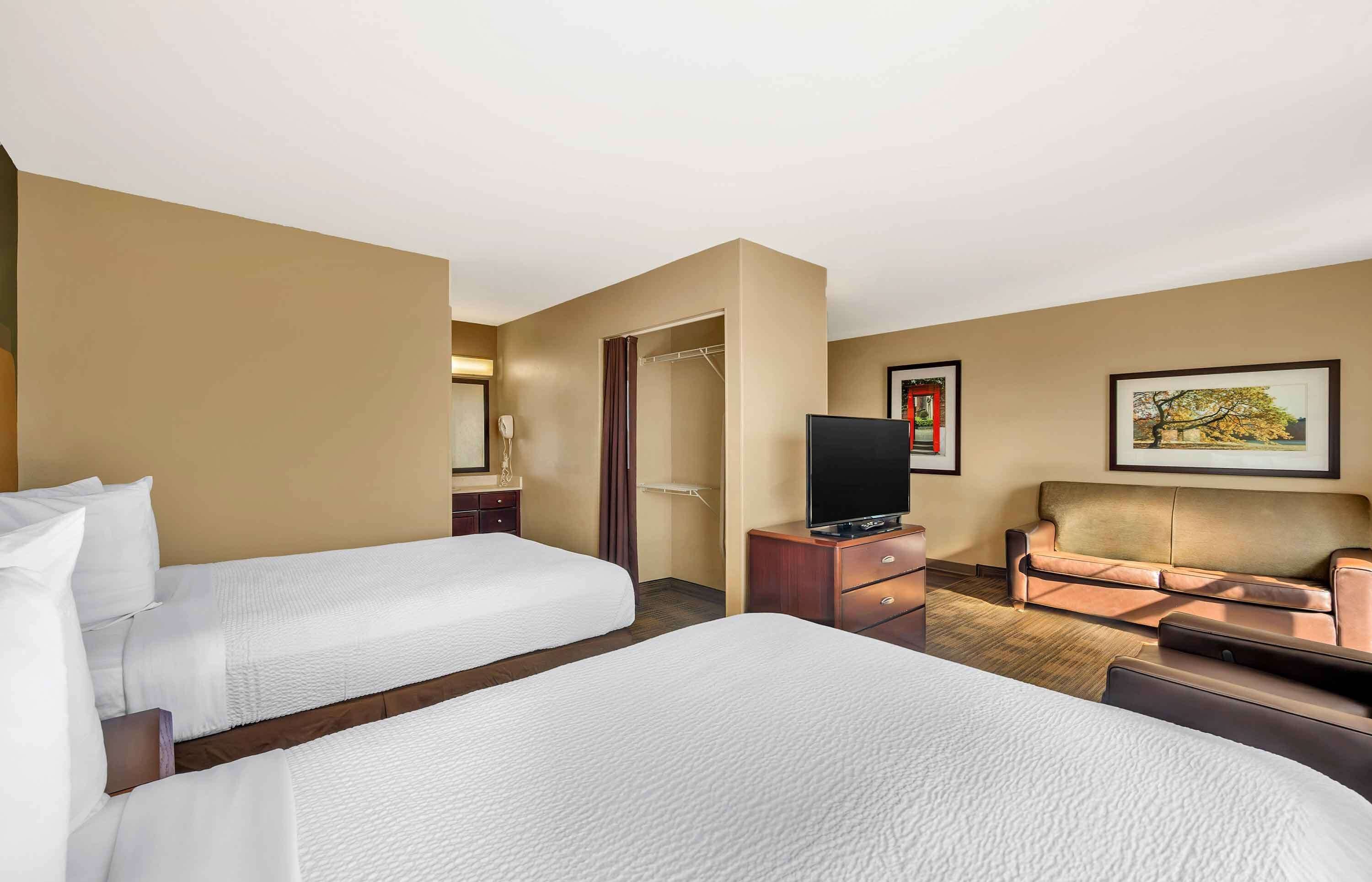 Habitación de hotel con dos camas, un televisor, un sofá y un cuadro en la pared.