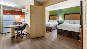 Ein Hotelzimmer mit einer Küchenzeile, zwei Betten, einem Schreibtisch mit Stuhl und einem Fernseher.