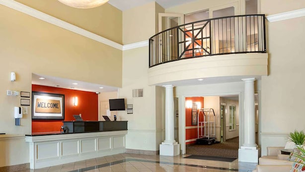 Eine Hotelhalle mit Empfangstresen, einem 'WELCOME'-Schild, einer Treppe und Blick in den Flur.