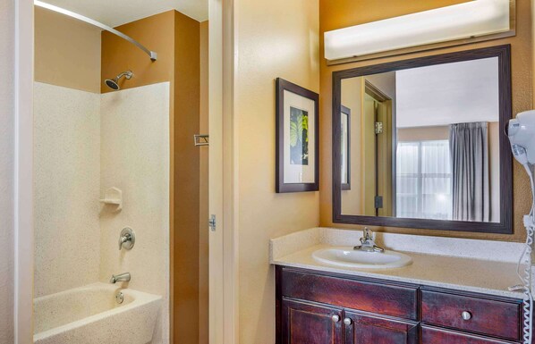 A bathroom with a bathtub, a sink, a vanity with drawers, a framed picture on the wall, and a large mirror above the sink.