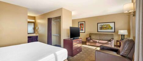 A hotel room with a large bed, a desk with a television, a sofa, a chair, and a small table with a lamp.