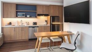 A modern kitchen with wooden cabinets, a microwave, a refrigerator, and a dining area with a table and chairs.